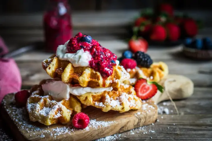 Pile de gaufres traditionnelles garnies de crème fouettée et de fruits rouges, saupoudrées de sucre glace. Un délice pour une recette de gaufre traditionnelle réussie.