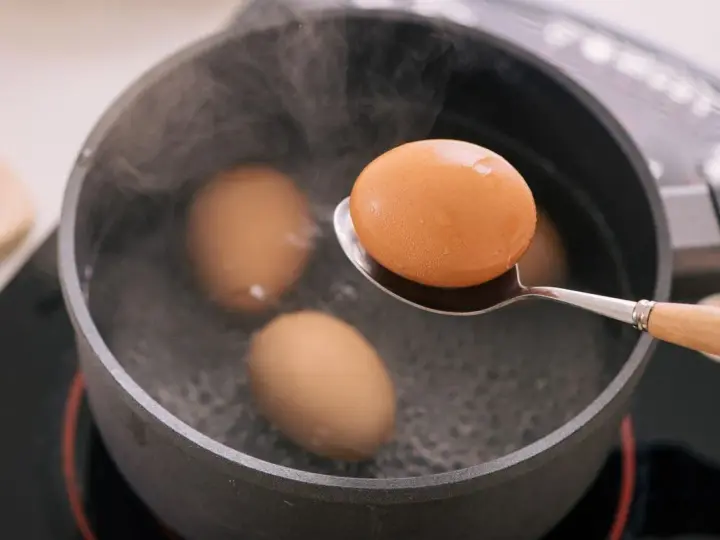 Un œuf mollet est retiré d'une casserole d'eau bouillante à l'aide d'une cuillère. La vapeur s'élève des œufs dans la casserole.