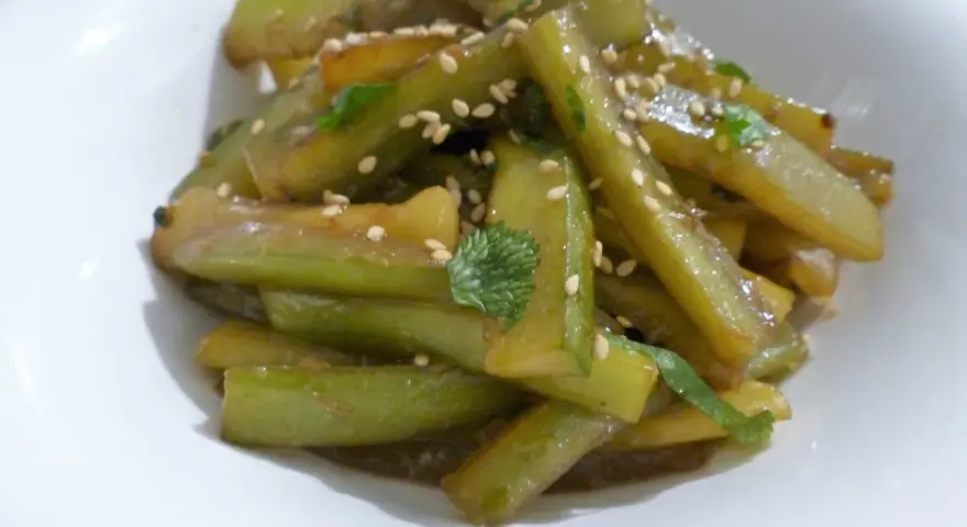 Délicieuse recette concombre cuit, garnie de graines de sésame et de persil frais, servie dans un bol blanc.