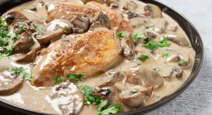 Un plat de poulet à la crème onctueuse, parsemé de champignons et de persil frais. Un délice crémeux qui invite à la dégustation.