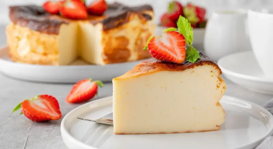 Tranche de gâteau au fromage brûlé, garnie de fraises et de menthe. Un dessert facile qui impressionne, parfait pour toute occasion.