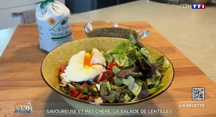Une assiette colorée de salade de lentilles garnie d'un œuf poché, de légumes frais et de tomates. Un sac de lentilles vertes est visible en arrière-plan.