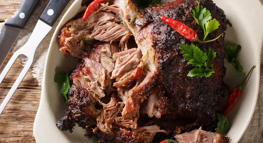 Gigot d'agneau au four cuisson lente, effiloché, garni de piments rouges et de persil frais. Un délice à partager.