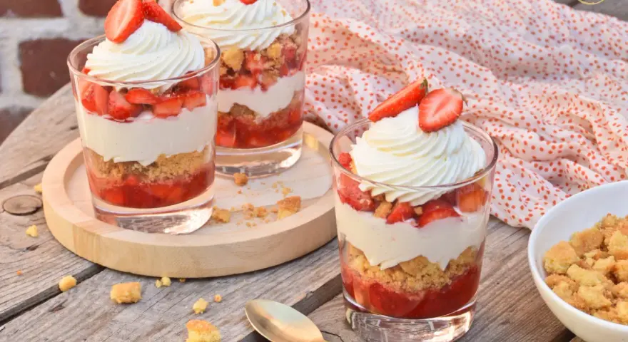 Trois verrines fraise mascarpone, garnies de crème fouettée et de fraises fraîches, sur une table en bois.