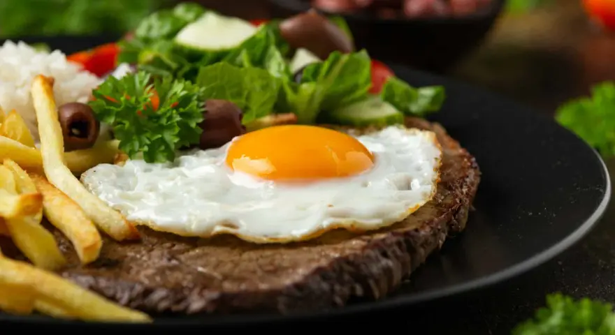 Un plat de steak a cheval savoureux avec un œuf au plat, des frites dorées, du riz blanc et une salade fraîche.