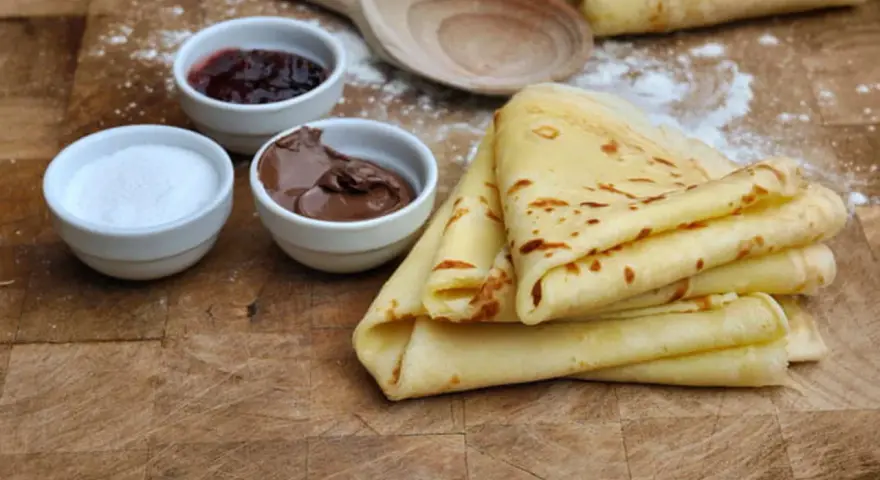 Crêpes dorées empilées, accompagnées de confiture, de pâte à tartiner au chocolat et de sucre. Un délice pour le petit-déjeuner ou le goûter.