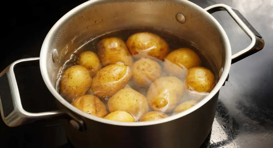 Pommes de terre entières dans une casserole d'eau bouillante, prêtes pour le temps de cuisson à l'eau.