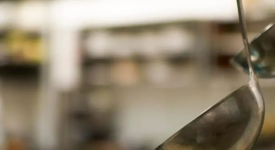 Deux louches en métal suspendues dans une cuisine. L'une est au premier plan, l'autre est floue en arrière-plan.