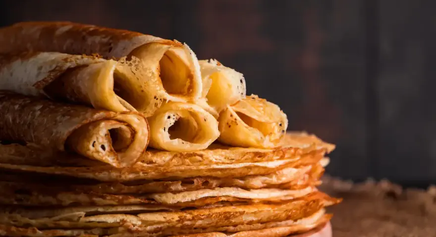 Pile de crêpes dorées, certaines roulées, prêtes à être dégustées. Une astuce pour garder les crêpes au chaud : les empiler ainsi !