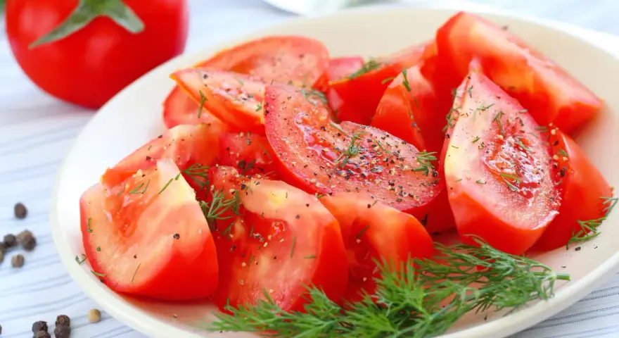 Une assiette de salade de tomates fraîches, assaisonnée de poivre noir et d'aneth. Un délice simple et coloré.