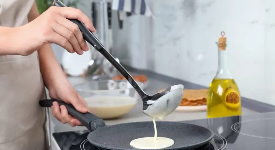 Une louche verse de la pâte à crêpes dans une poêle. On dirait qu'il y a trop de beurre dans la pâte à crêpes, elle est très liquide !