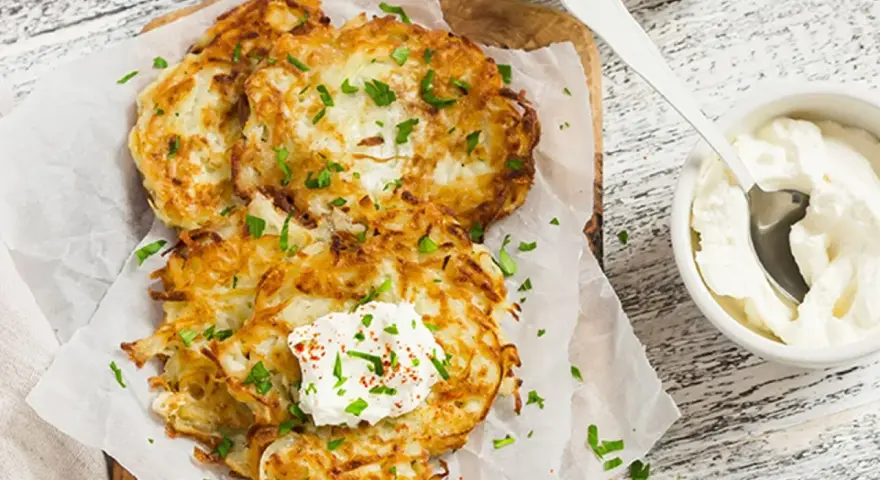 Délicieux rapé de pomme de terre doré, garni de crème fraîche et de persil, prêt à être dégusté avec une touche de paprika.