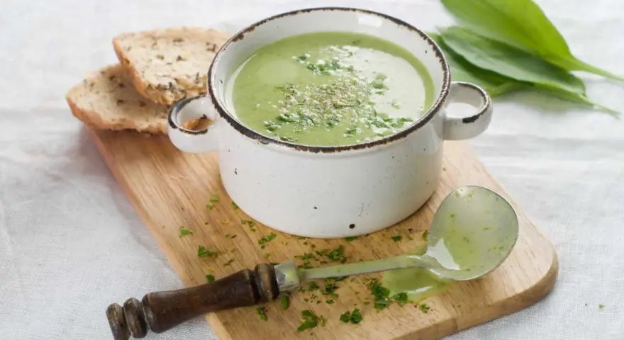 Délicieuse soupe courgette verte, garnie d'herbes fraîches, servie avec du pain grillé et une louche.