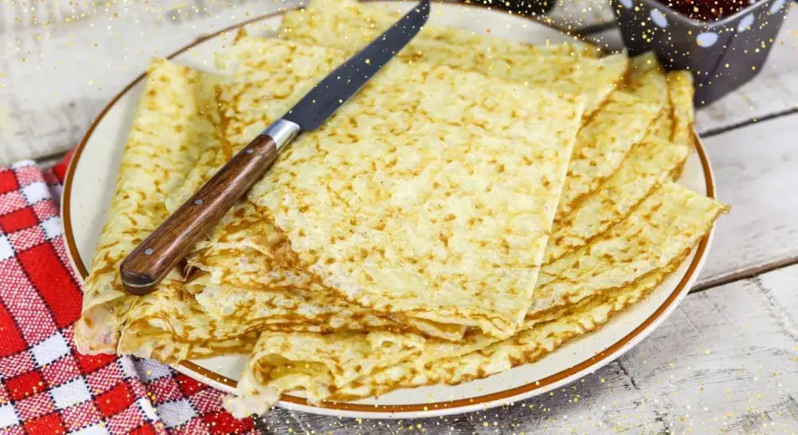 Pile de crêpes bretonnes dorées sur une assiette, prêtes à être dégustées. Un couteau est posé dessus.