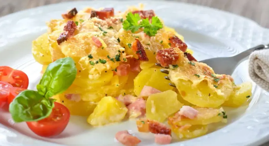 Un délicieux gratin de pommes de terre et lardons, doré au four, servi avec des tomates cerises et du basilic. Un plat réconfortant et savoureux.