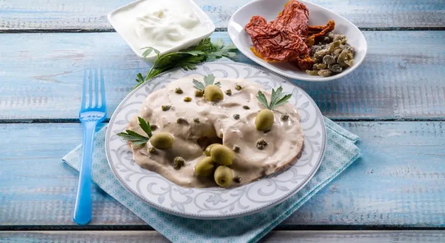 Tête de veau en sauce crémeuse, garnie d'olives et de câpres, accompagnée de tomates séchées et de yaourt.