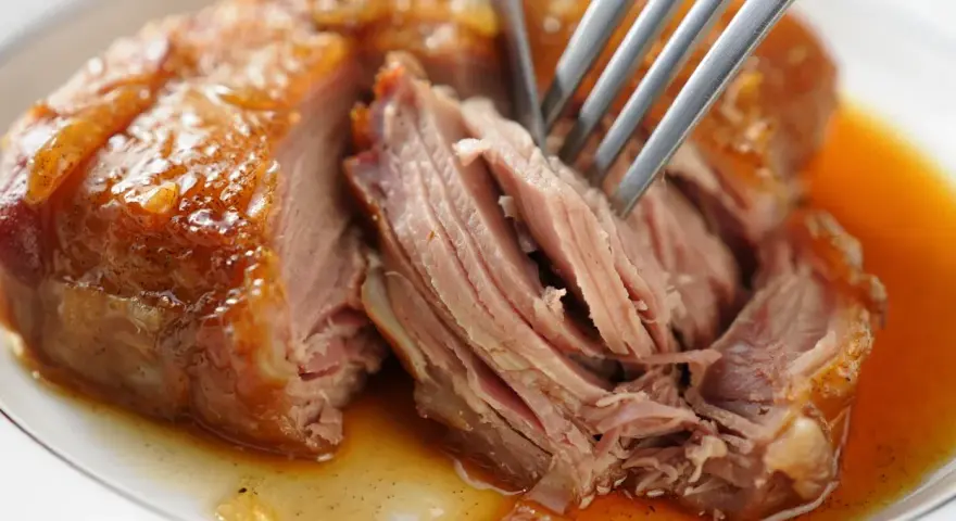 Une rouelle de porc au four, tendre et juteuse, est effilochée à la fourchette dans son jus doré.