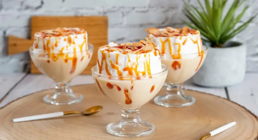 Trois coupes de crème anglaise avec une île flottante meringuée, nappées de caramel et d'amandes effilées.