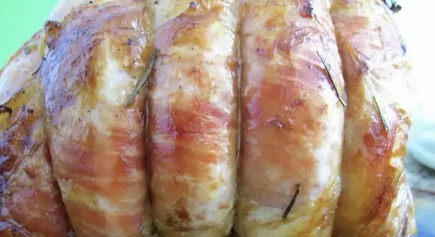 Un délicieux roti de veau, enveloppé de lard et parsemé de romarin, prêt à être dégusté.