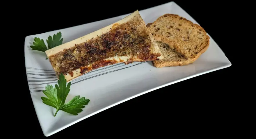Un os à moelle rôti, assaisonné et garni de persil, servi avec des toasts grillés sur une assiette blanche.