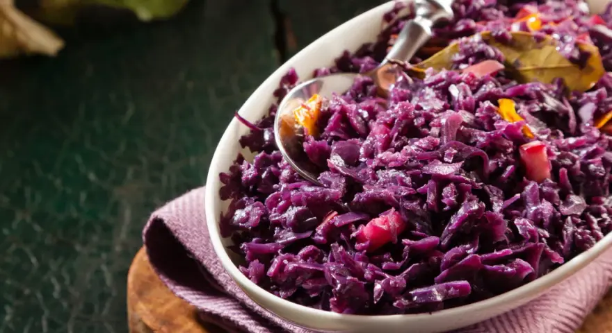 Un plat de chou rouge recette, cuisiné avec des épices et des morceaux de pomme, servi dans un bol blanc.