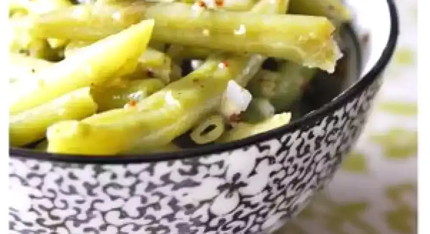 Salade de haricots verts croquants, assaisonnée et parsemée de quelques épices rouges, servie dans un bol décoratif.