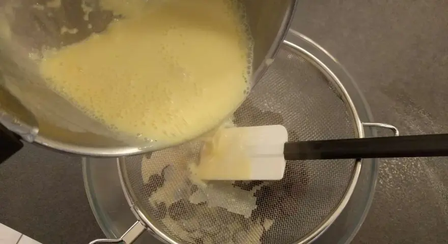 Verser la crème anglaise à travers une passoire fine pour obtenir une texture lisse.