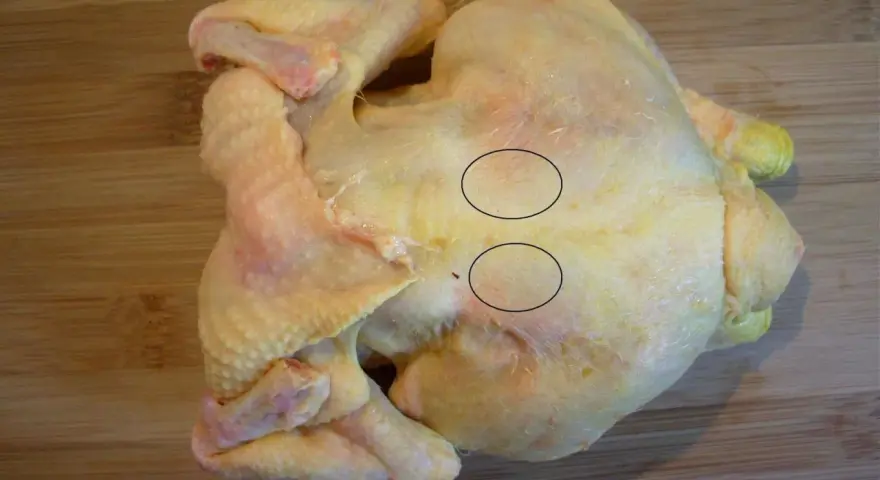 Un poulet cru sur une planche à découper en bois. Deux cercles noirs entourent des zones de chair où l'on voit des fibres musculaires. On dirait que le sot l'y laisse.