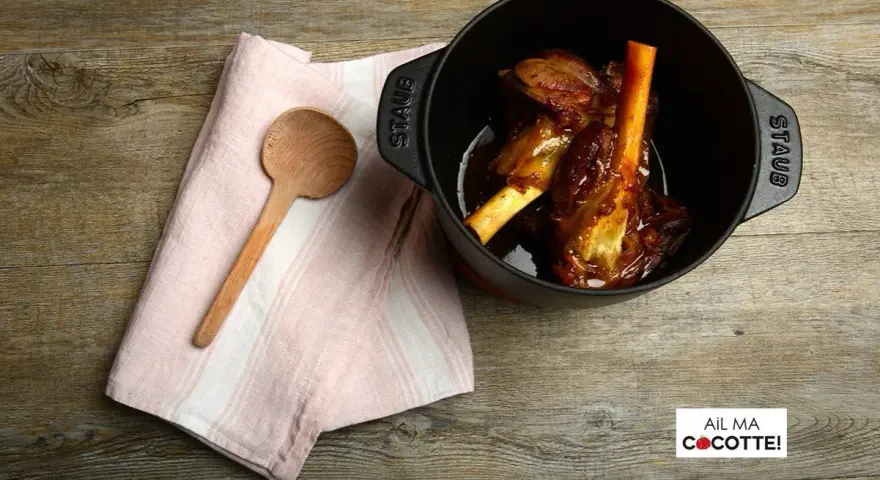 Souris d'agneau à la cocotte en fonte, tendres et savoureuses, prêtes à être dégustées. Une cuillère en bois et une serviette rose complètent la scène.