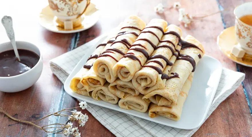 Crêpes roulées, nappées de chocolat, accompagnées d'une tasse de thé. Une recette crêpe raffinée pour un goûter gourmand.