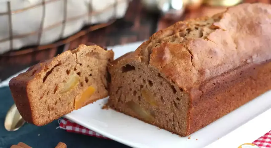 Un délicieux pain d'épices aux fruits confits, coupé en deux, sur une assiette blanche. Des bâtons de cannelle et des décorations de Noël en arrière-plan.