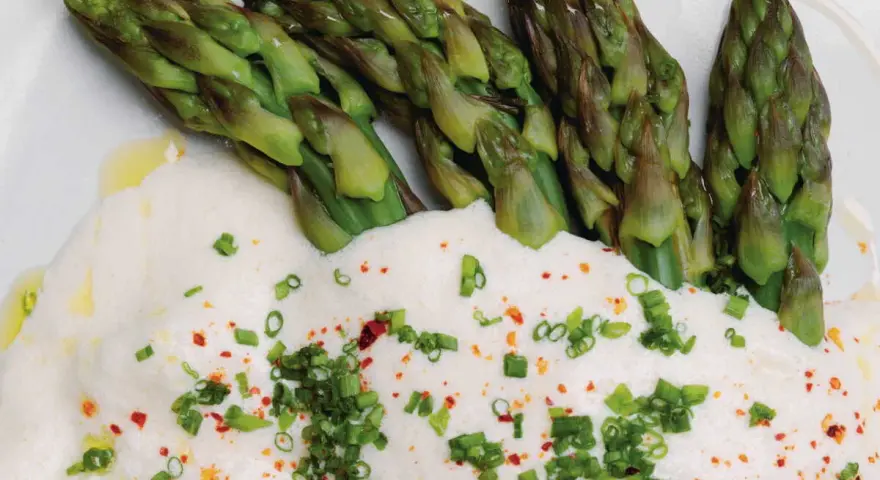 Asperges vertes tendres nappées d'une onctueuse sauce mousseline, parsemées de ciboule et de piment. Un délice printanier.