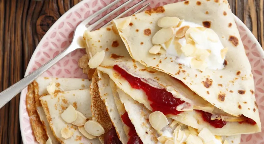 Crêpes fines garnies de confiture et de crème, parsemées d'amandes effilées. Une délicieuse recette crêpe sans beurre pour un goûter léger.