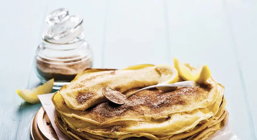 Pile de crêpes au lait entier, saupoudrées de sucre et de cannelle, garnies de quartiers de citron. Un délice simple et gourmand.