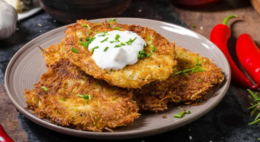 Trois galettes de pomme de terre dorées et croustillantes, garnies de crème aigre et de ciboulette, sur une assiette.