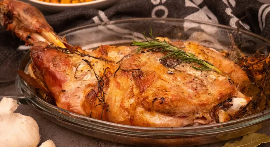 Une succulente épaule d'agneau rôtie à la perfection, garnie de romarin frais, prête à être dégustée.