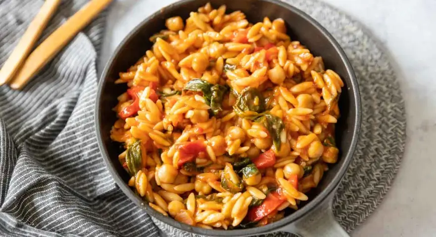 Un plat de cuisson orzo savoureux avec des pois chiches, des poivrons rouges et des épinards dans une sauce tomate.