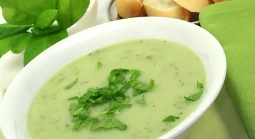 Un bol de soupe à l'oseille crémeuse, garnie d'herbes fraîches, avec du pain en arrière-plan.