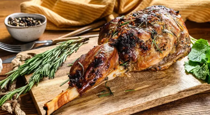 Gigot d'agneau rôti, doré et savoureux, garni de romarin et de moutarde, prêt à être dégusté.