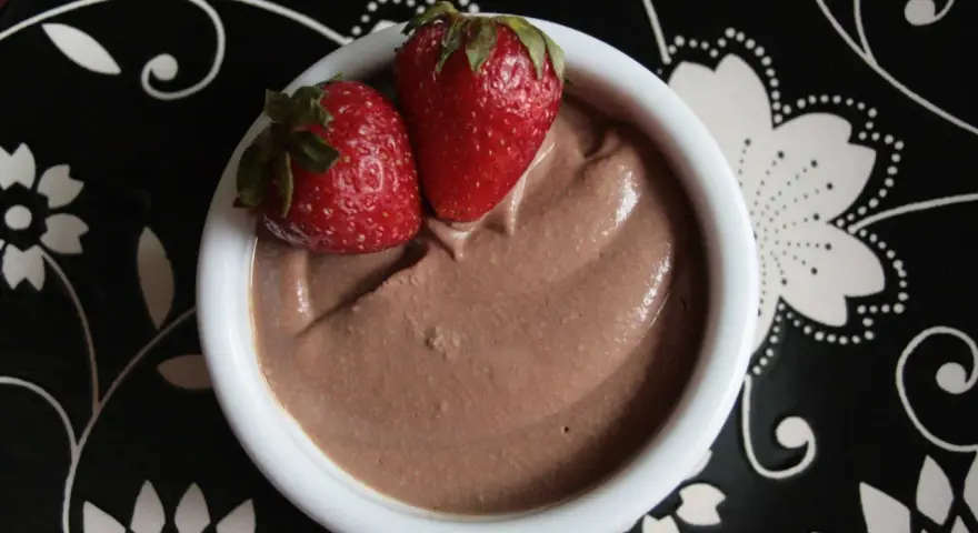 Délicieuse crème au chocolat onctueuse, garnie de deux fraises fraîches, servie dans un bol blanc sur une assiette noire décorée.