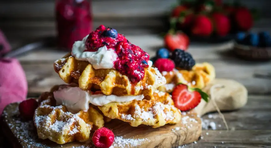 Pile de gaufres traditionnelles garnies de crème fouettée et de fruits rouges, saupoudrées de sucre glace. Un délice pour une recette de gaufre traditionnelle réussie.