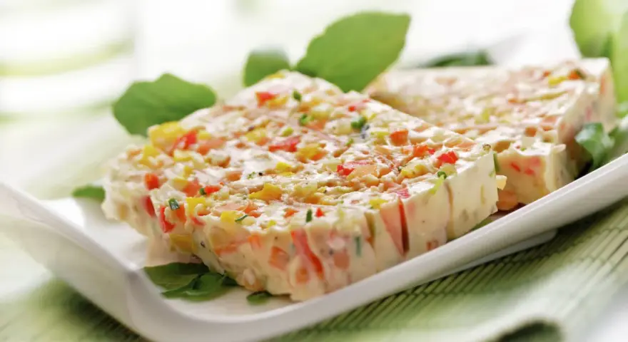 Tranches de terrine de légumes colorée, garnie de feuilles vertes, sur une assiette blanche.