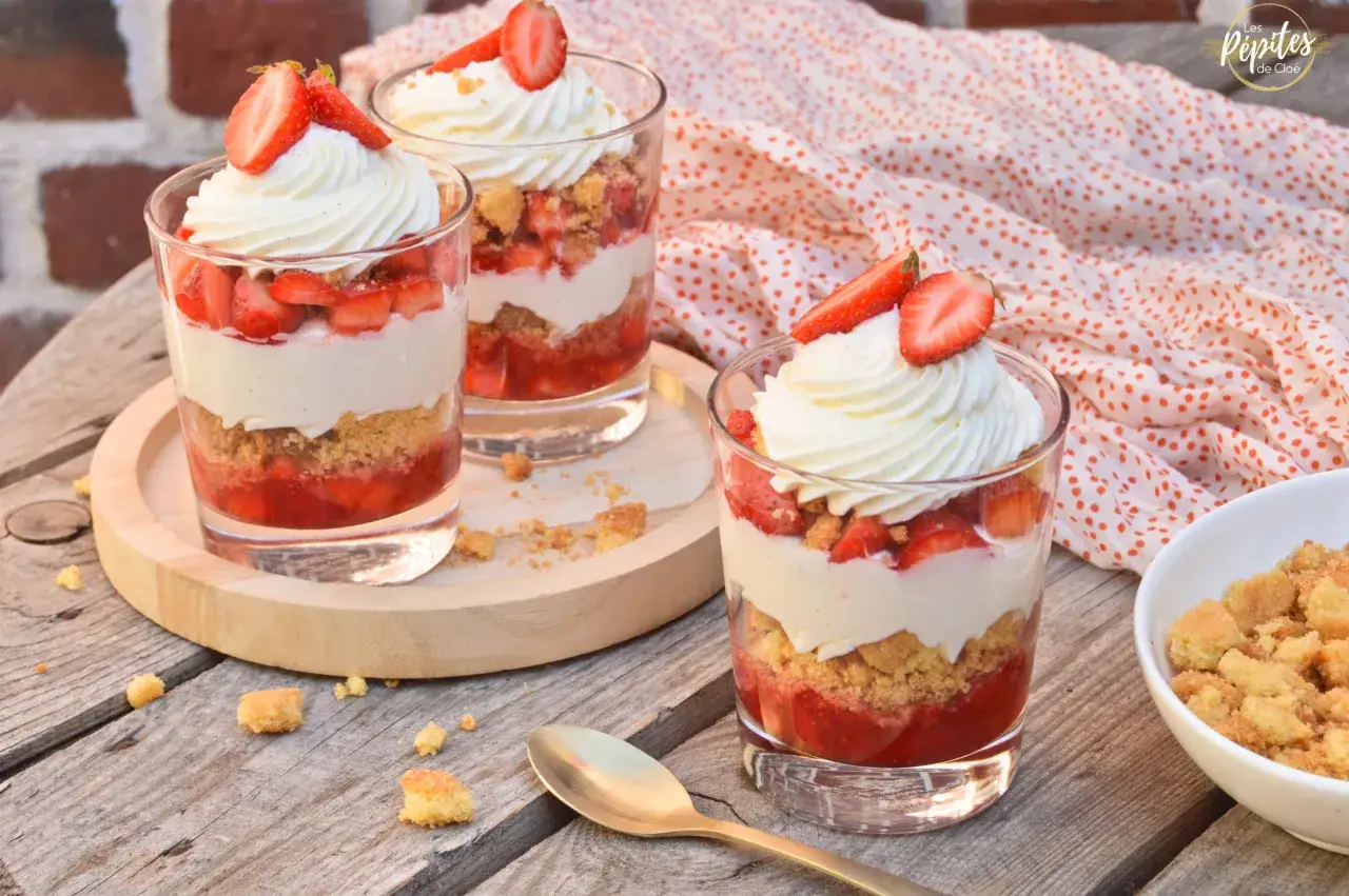 Trois verrines fraise mascarpone, garnies de crème fouettée et de fraises fraîches, sur une table en bois.