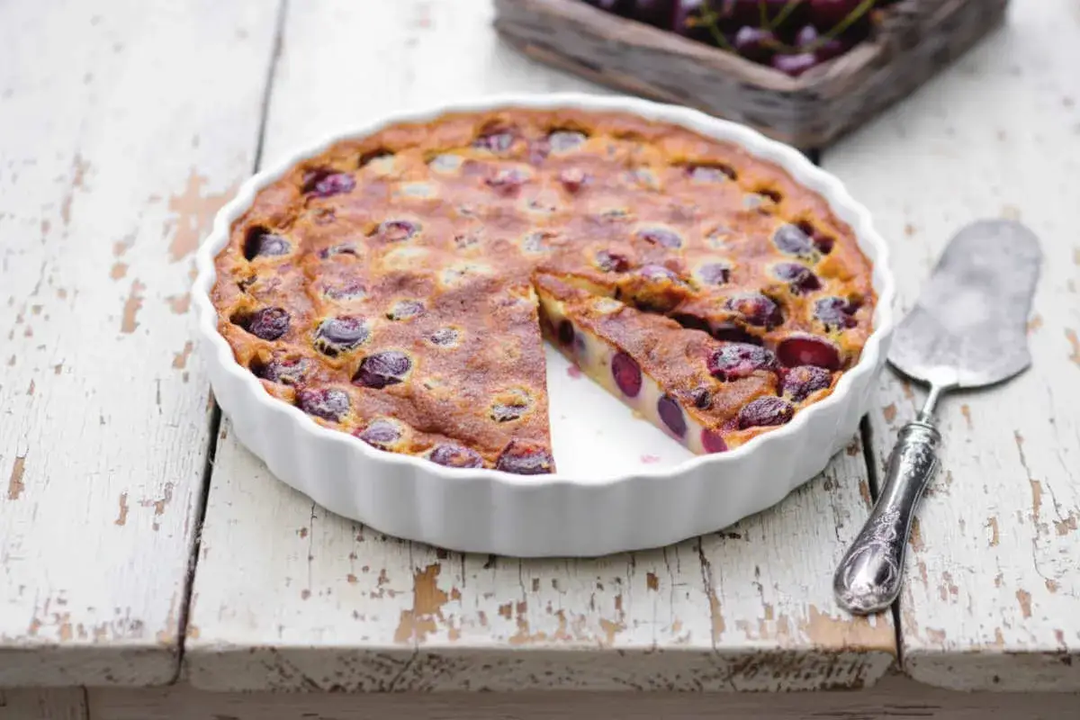 Un délicieux clafoutis aux cerises, tout juste sorti du four, avec une part coupée pour révéler sa texture moelleuse et ses fruits juteux.