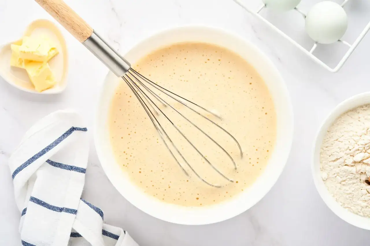 Un fouet métallique dans un bol de pâte à crêpes lisse, prêt à montrer comment enlever les grumeaux d'une pâte à crêpes.