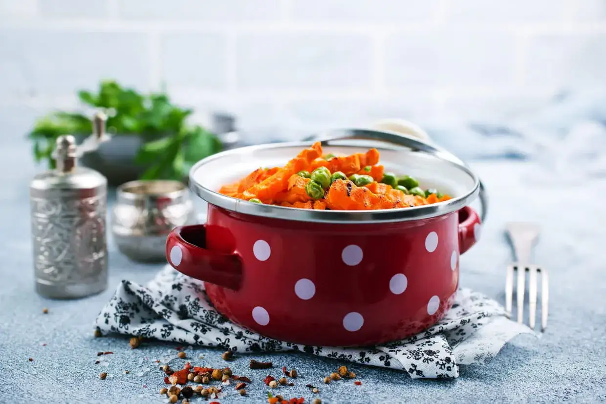 Carottes et petits pois dans une cocotte rouge &agrave; pois blancs, pr&ecirc;ts pour la cuisson vapeur.