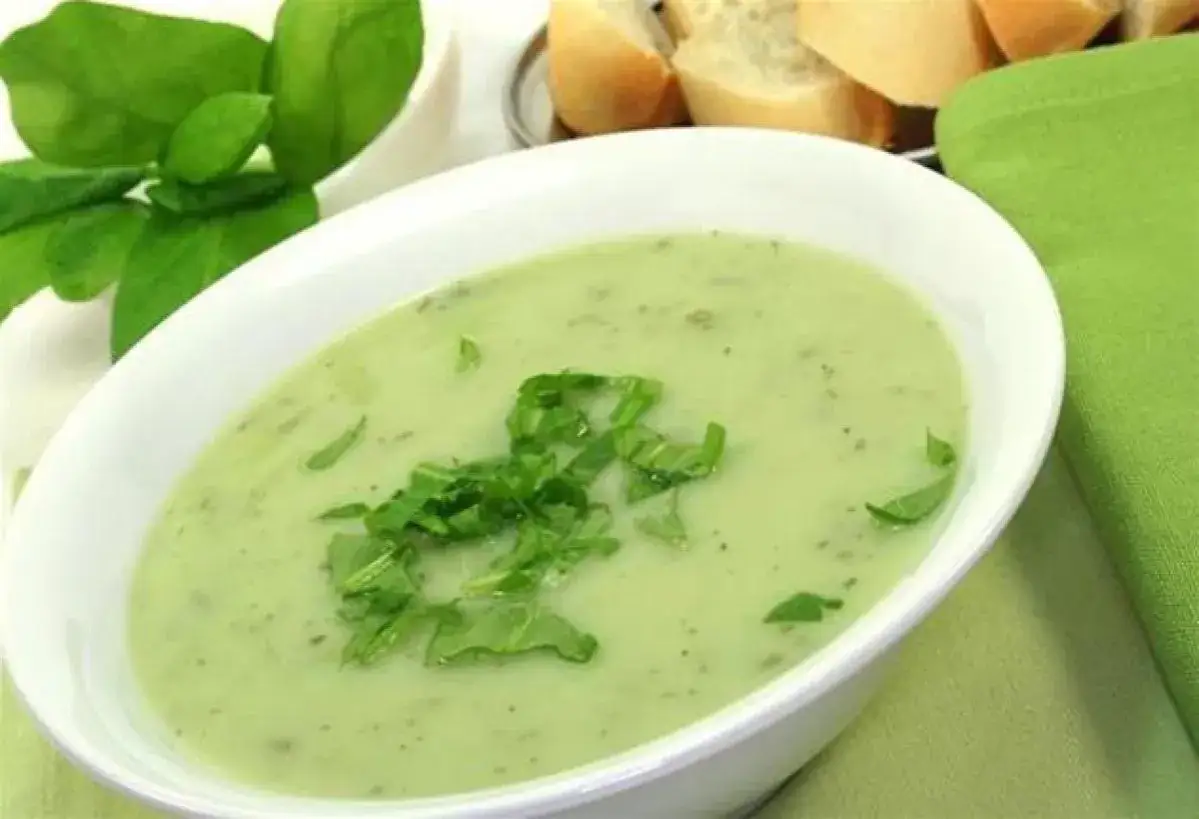 Un bol de soupe à l'oseille crémeuse, garnie d'herbes fraîches, avec du pain et une serviette verte en arrière-plan.