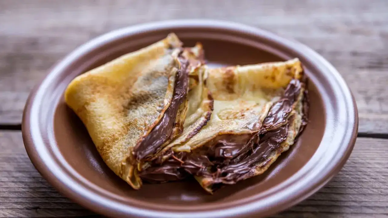 Cr&ecirc;pes garnies de nutella liquide pour cr&ecirc;pe, sur une assiette marron.