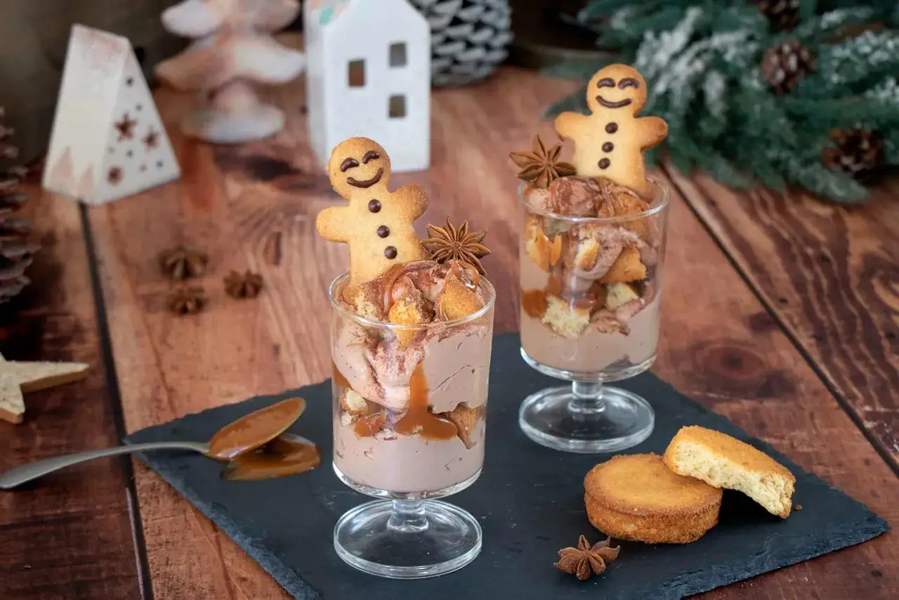 Deux coupes de mousse au chocolat au lait, garnies de biscuits bonhomme pain d'épice et de caramel. Ambiance festive.