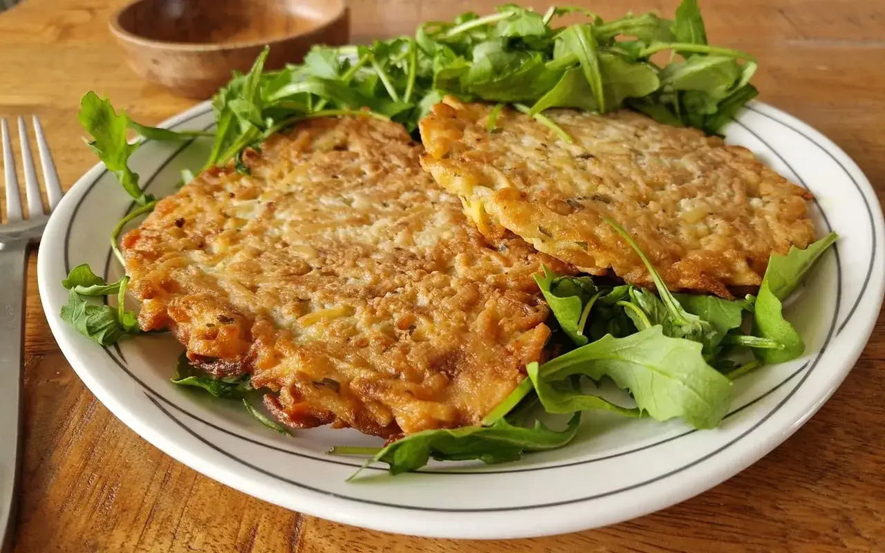 Deux galettes dor&eacute;es de rap&eacute; de pomme de terre, garnies de roquette fra&icirc;che, sur une assiette blanche &agrave; rayures grises.